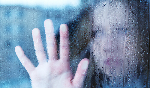 Kvinde sætter hånd mod vådt vindue