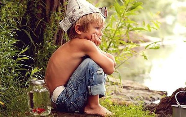 En dreng sidder på hug med avishat på