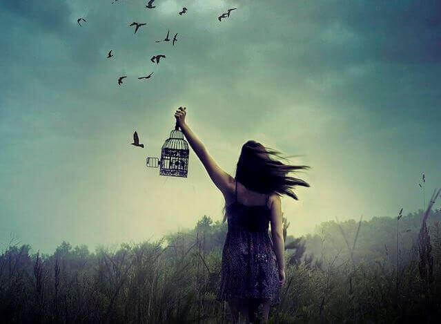 En kvinde holder et fuglebur og slipper fuglene fri