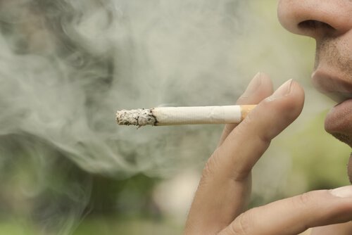 Fingre holder en cigaret med røg omkring