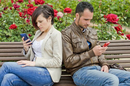 Et par sidder med ryggen mod hinanden og kigger på hver deres telefoner, som er en af nutidens forholds forhindringer