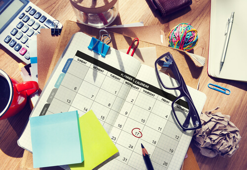 Et skrivebord med en kalender, briller og notesblok