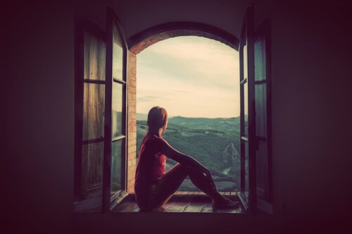 En kvinde sidder i et vindue og kigger ud på landskabet