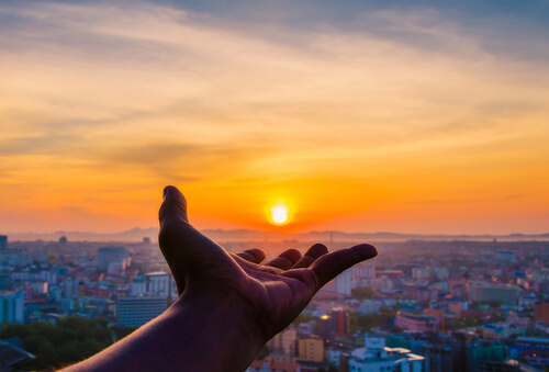 En hånd rækker ud mod en solnedgang som symbil på, at man skal værdsætte det, man har