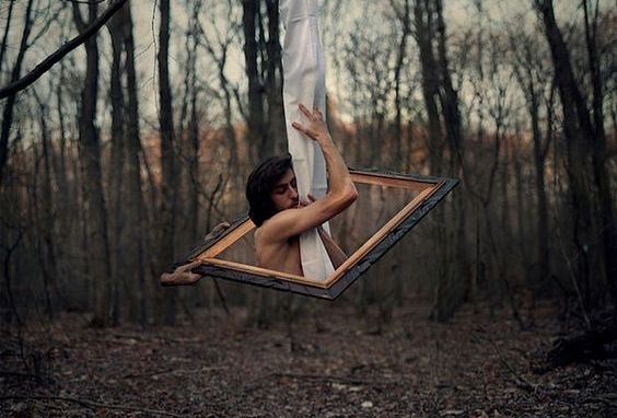 Mand i en ramme i en skov klynger sig til et stykke stof og prøver at værdsætte det, han har