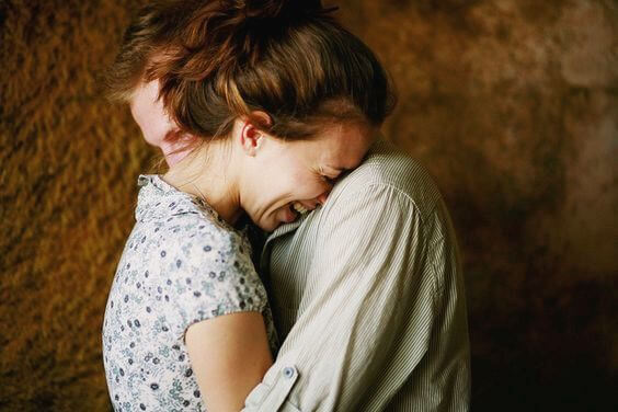 Kvinde græder ud ved mands skulder, som giver social støtte