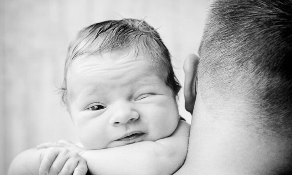 En baby ligger på sin fars skulder med et øje åbent for at illustrere spædbarnets syn
