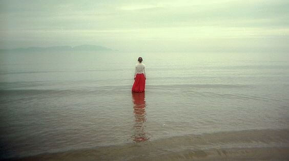 Kvinde med lang rød nederdel står ved hav