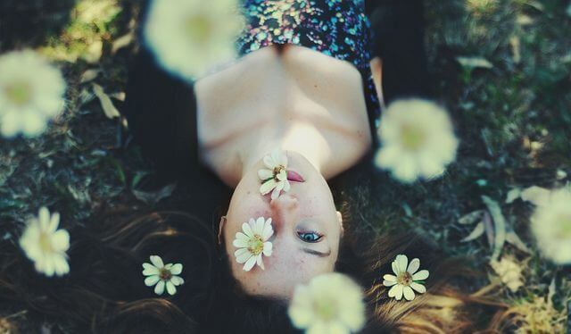 Kvinde ligger på jord med blomster over sig