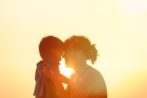 Mor og barn krammer foran sol