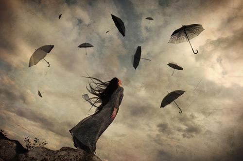 Kvinde kigger op på stormfuld himmel med flyvende paraplyer