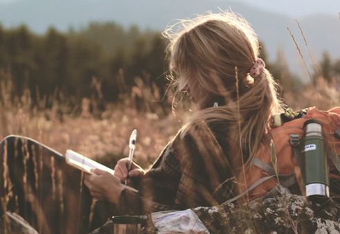 Kvinde sidder på mark og skriver og nyder lykke