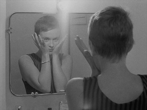 Kvinde tager hænderne væk fra sit ansigt, ser sig selv i spejlet og overvejer spejlets lov