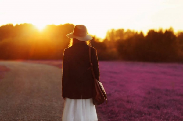 Kvinde med hat på blomstermark foran solnedgang