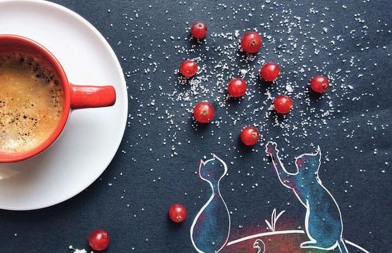 En kop kaffe og en tegning af to katte på bordet