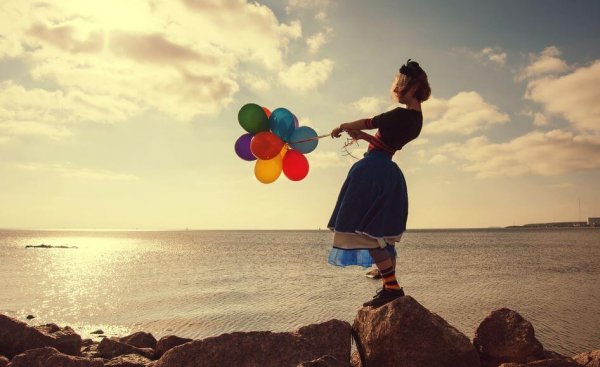 Kvinde ved hav prøver at holde fast i balloner