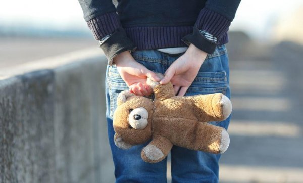 Barn står med bamse bag ryggen