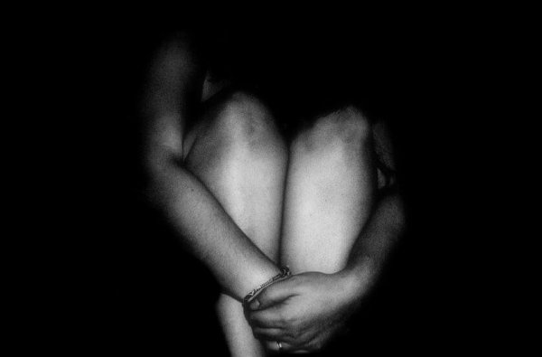 Person sidder i mørke og holder om sine ben