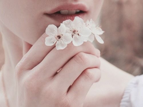 Hvide blomster foran mund på kvinde, der er minimalist og værdsætter de små ting