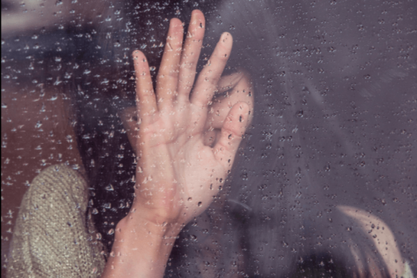 Kvinde sætter hånd op på rude med regn på