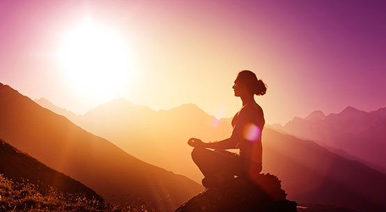Person på bjerg ved solopgang anvender mantraer til meditation