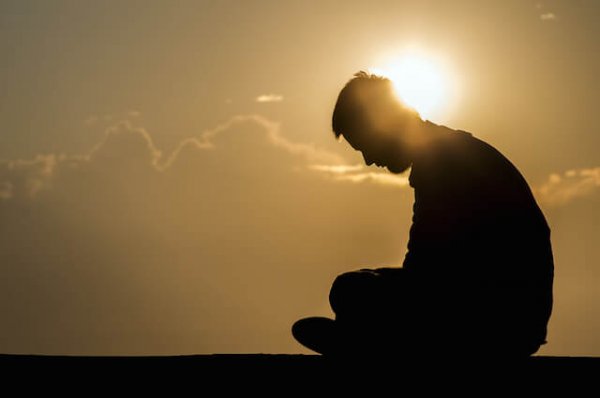 Person sidder med bøjet hoved foran sol, trist over passiv vold