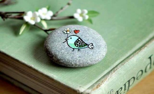Fugl malet på sten bærer blomst