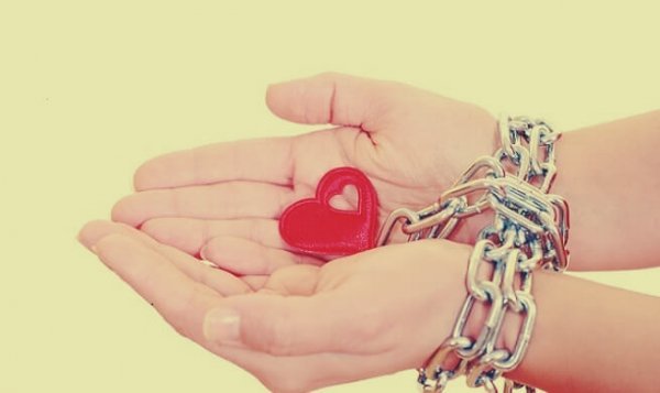 Hjerte er låst fast i hænder med kæder som symbol på falsk kærlighed