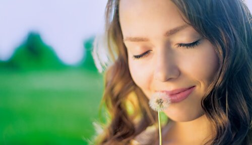 Kvinde smiler og dufter til blomst