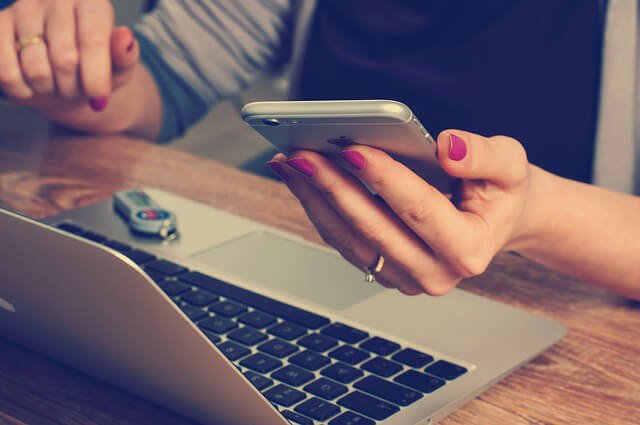Kvinde tjekker telefon mens hun sidder ved computer