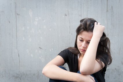 Trist kvinde foran grå væg lider af tilpasningslidelse