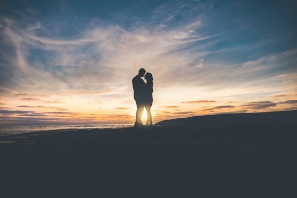 Par står tæt foran skyer og solnedgang og nyder resultater af sunde tilknytningsmønstre