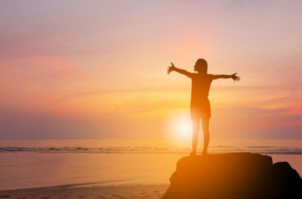 Kvinde på klippe foran solopgang nyder følelsen af serotonin og dopamin