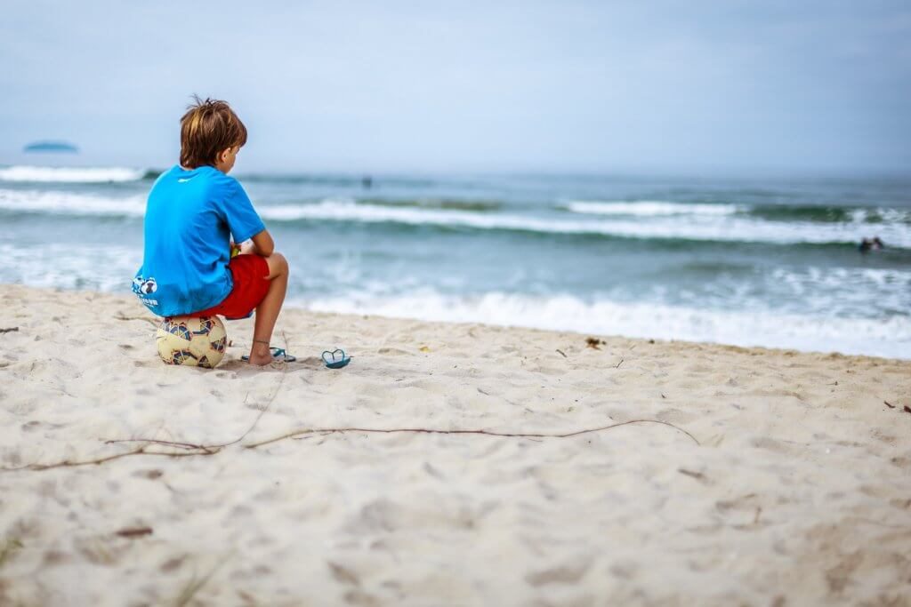 Barn sidder alene på strand og kigger ud på horisonten