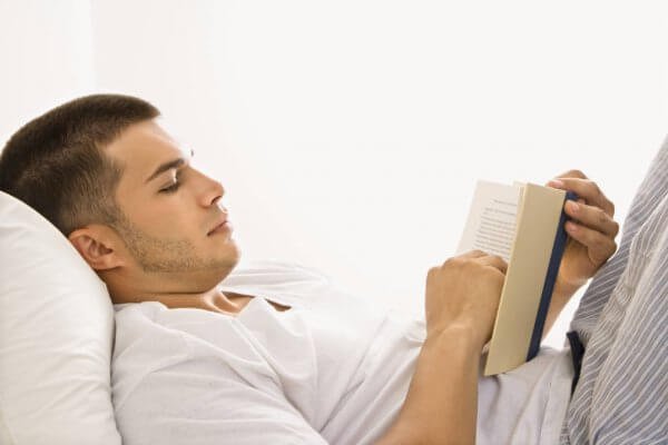 Mand med bog i seng nyder at læse før sengetid