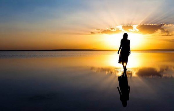 Kvinde går mod sol på strand for at genvinde positiv energi