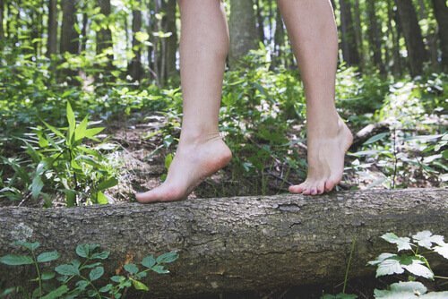 Kvinde går barfodet på træstamme og nyder en af de usædvanlige vaner med at gå i naturen