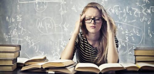 Kvinde sidder foran mange bøger og tager sig til hoved