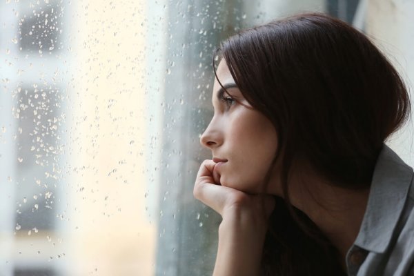 En trist kvinde stirrer ud af et regnfuldt vindue. messias fælden