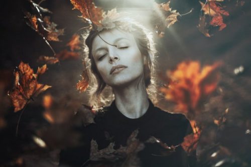 Kvinde står i en skov med efterårs bladene omkring sig