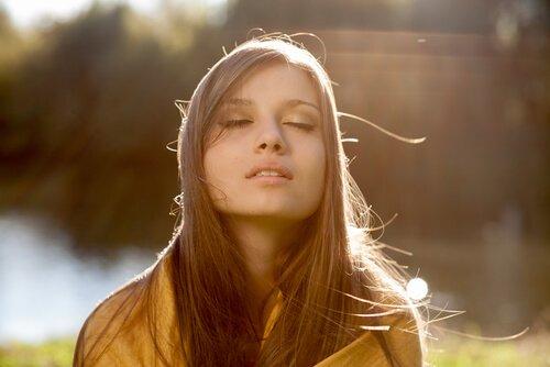 Kvinde står med lukkede øjne mod solen