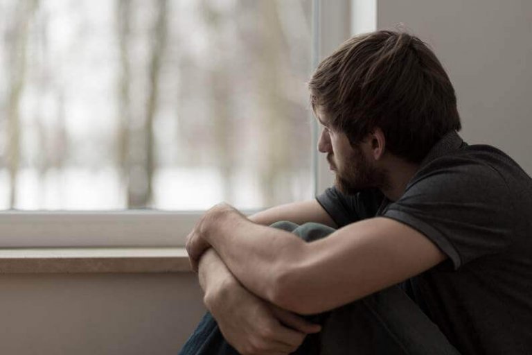 Trist mand ser ud af vindue og oplever ufrivillig ensomhed
