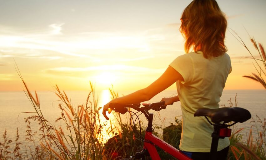 Kvinde med cykel foran solopgang