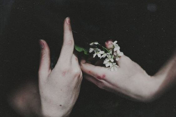 Blodige hænder holder blomster og illustrerer selvdestruktive mennesker