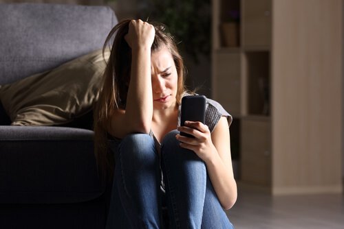 Kvinde græder med telefon i hånden som følge af postmoderne ensomhed