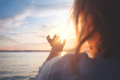 Kvinde rækker hånden ud mod sol ved hav