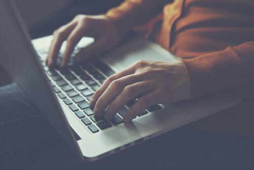 Kvinde sidder med sin computer på skødet og er plaget af teknostress