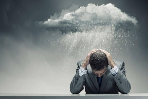 Mand sidder med hænderne på hovedet og en regnsky over sig