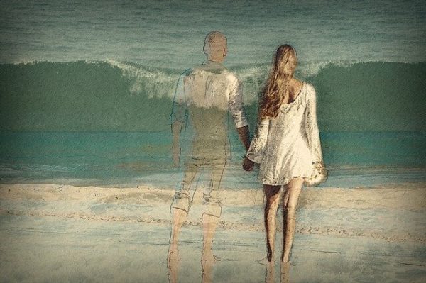 Kvinde står med silhuet af mand foran hav