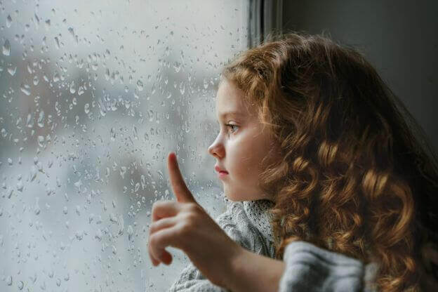 Lille pige ser på regn på vindue